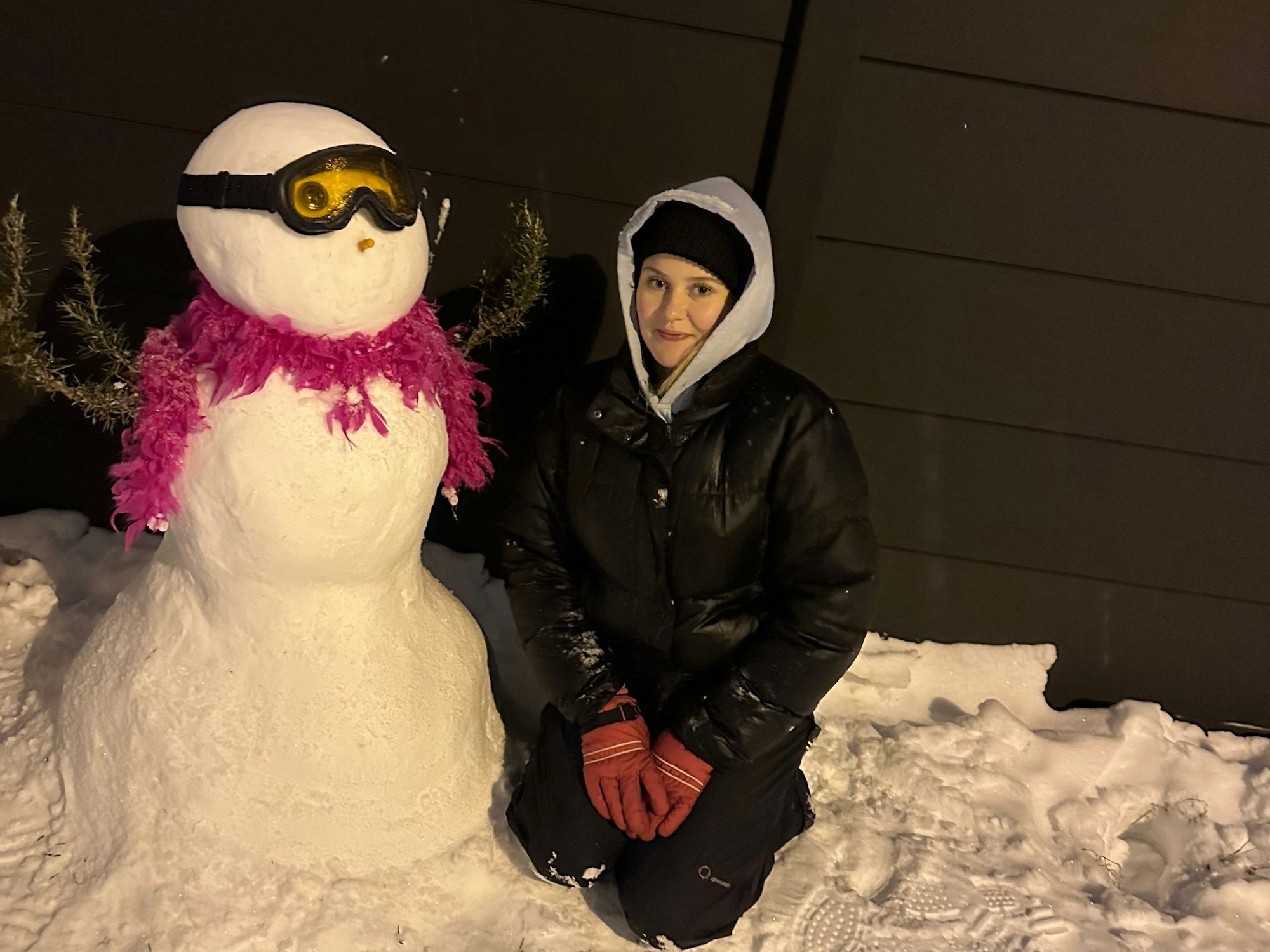 Eine Frau hockt neben einem Schneemann.