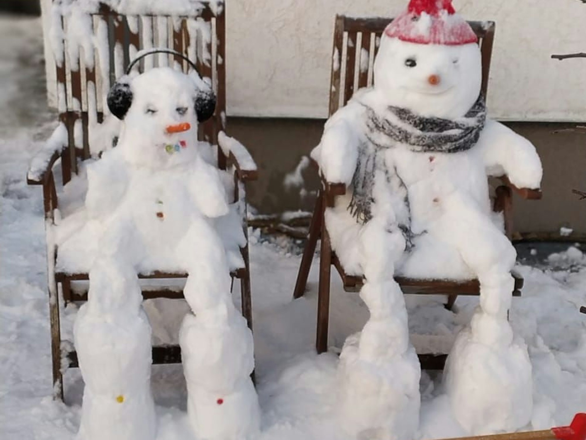 Zwei Schneemänner sitzen auf Holzstühlen.