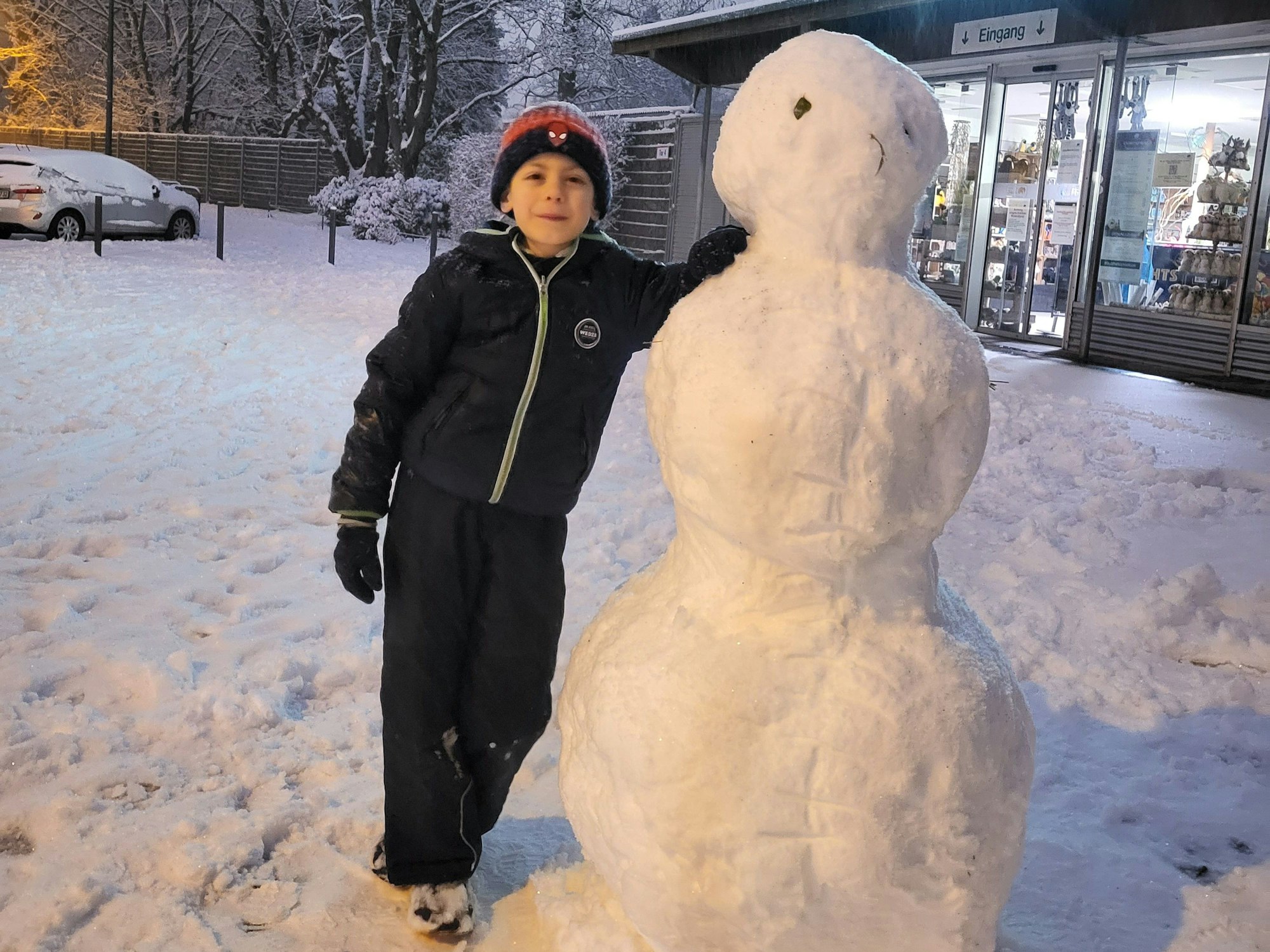 Ein Junge steht neben einem Schneemann.