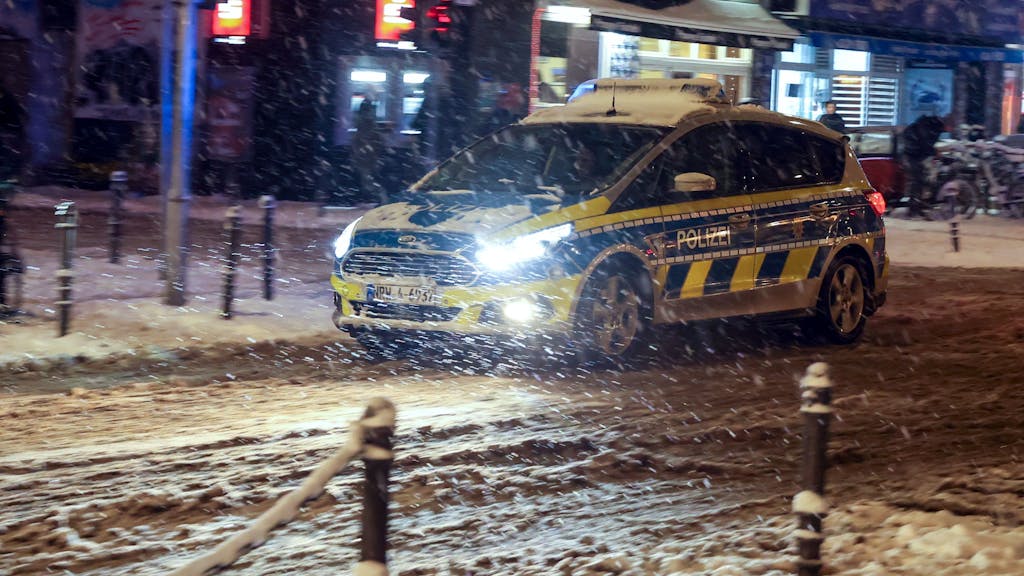 Ein Polizeifahrzeug fährt über die zugeschneite Venloer Straße.






