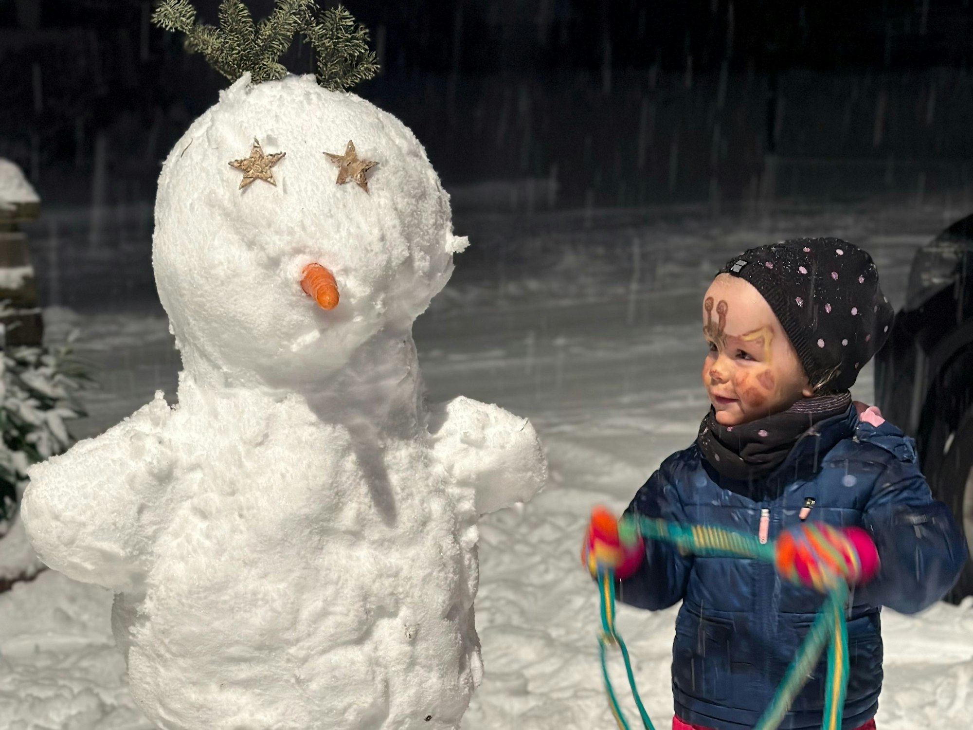 Ein Kind steht neben einem Schneemann.
