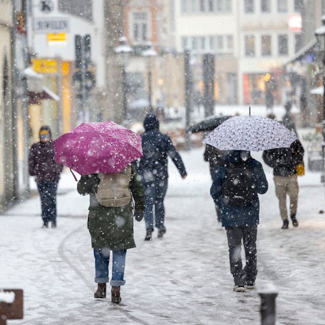 Menschen gehen bei dichtem Schneefall durch die Bonner Innenstadt.
