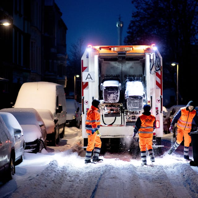 Ein Müllwagen fährt über eine zugeschneite Straße.&nbsp;