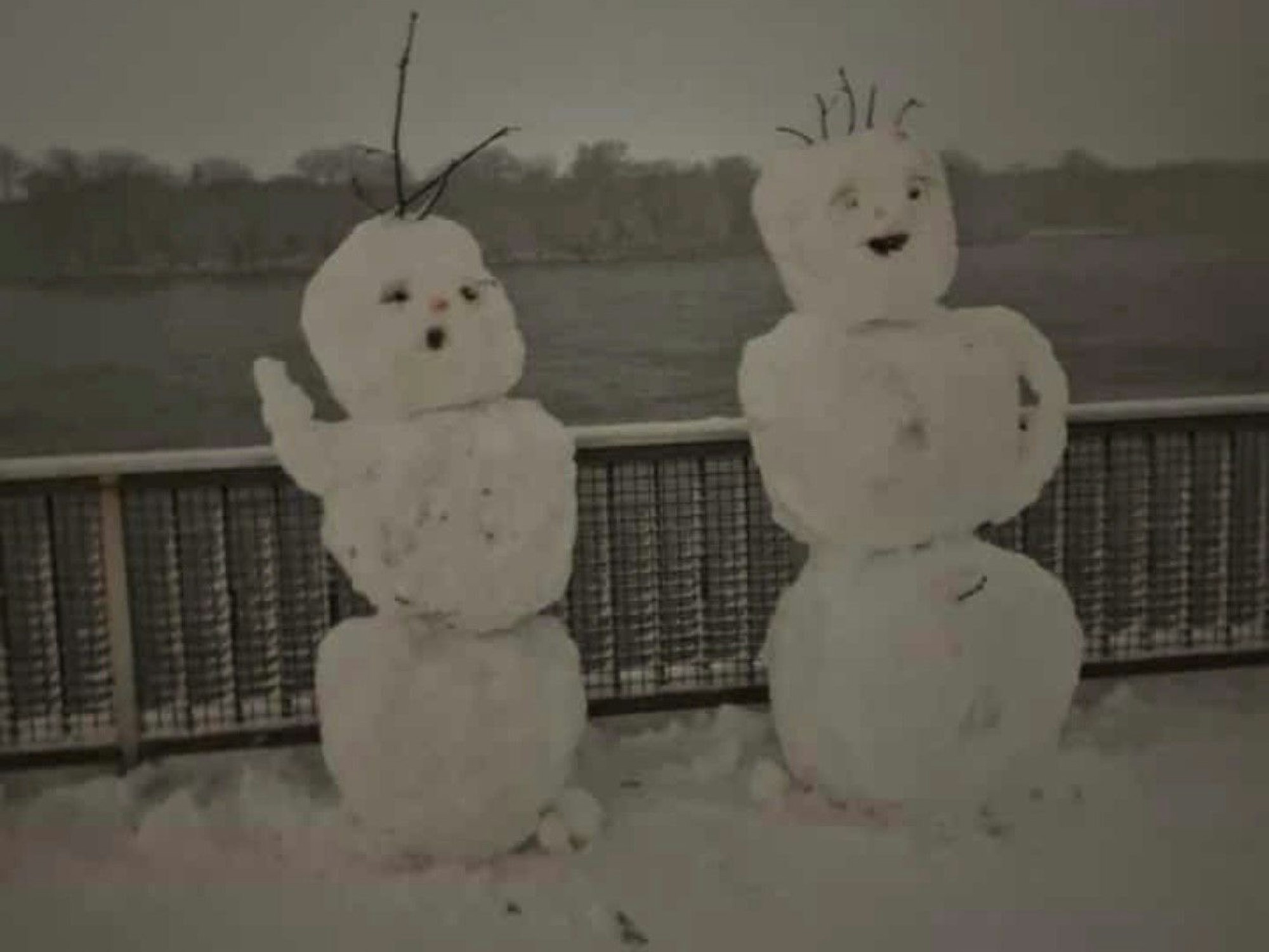 Zwei Schneemänner stehen auf einem Gehweg.
