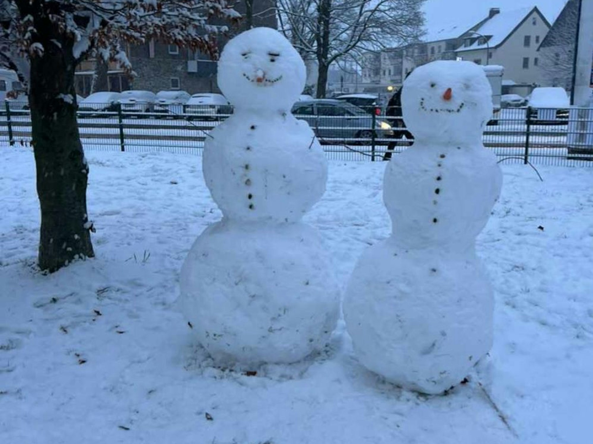 Zwei Schneemänner stehen in einem Park.