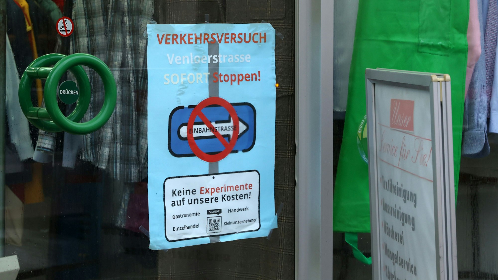 Ein Schild mit der Forderung, den Verkehrsversuch zu stoppen, hängt in einem Schaufenster an der Venloer Straße.