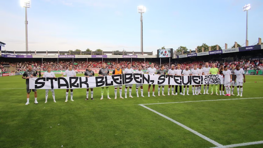 Die Mannschaft von Borussia Mönchengladbach hält ein Banner mit der Aufschrift „Stark bleiben, Stevie!“.