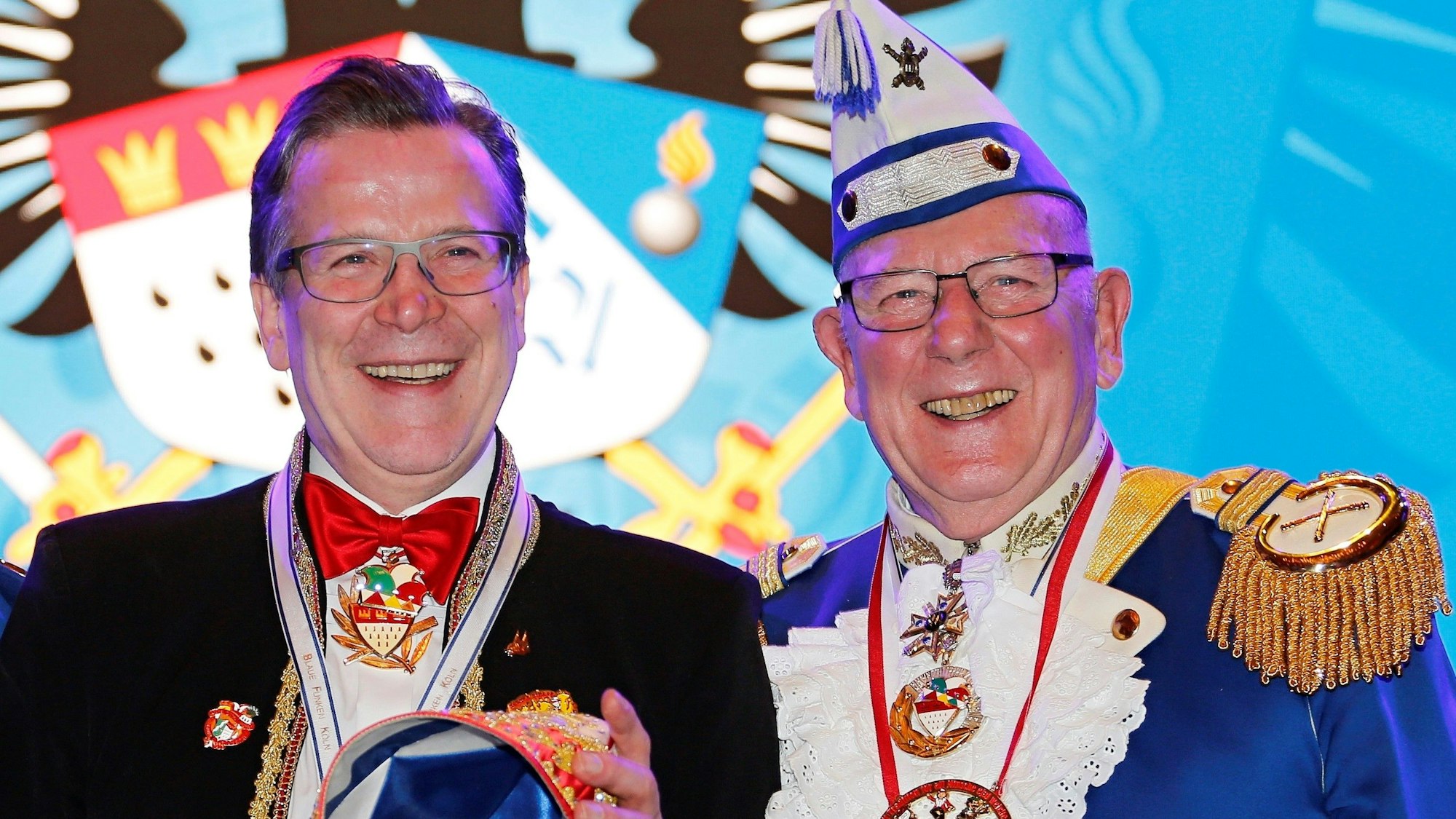 Christoph und Fro Kuckelkorn in Karnevals-Outfits auf einer Bühne, beide lächeln.