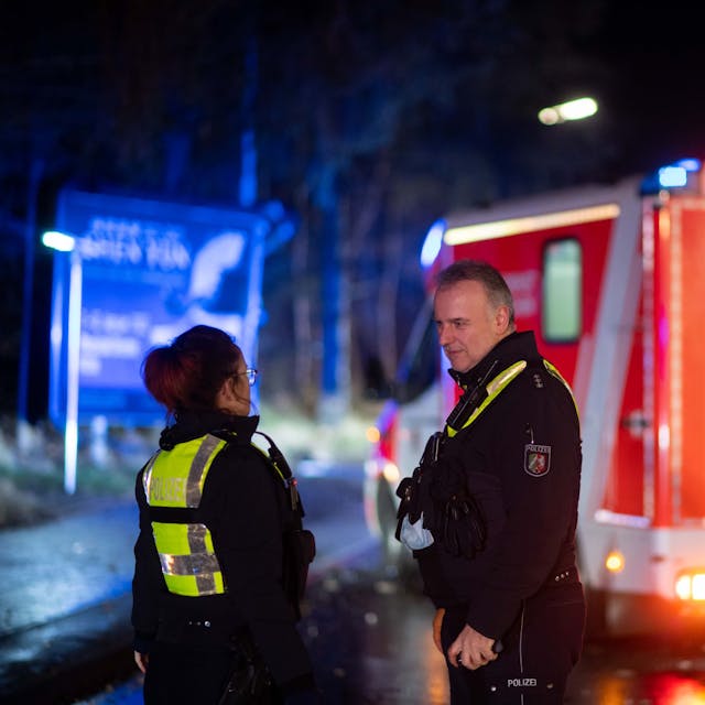 Zwei Polizisten stehen bei einem Einsatz in der Dunkelheit vor einem Rettungswagen.