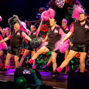 Männer in Cheerleader-Uniformen tanzen mit Pom-Poms.
