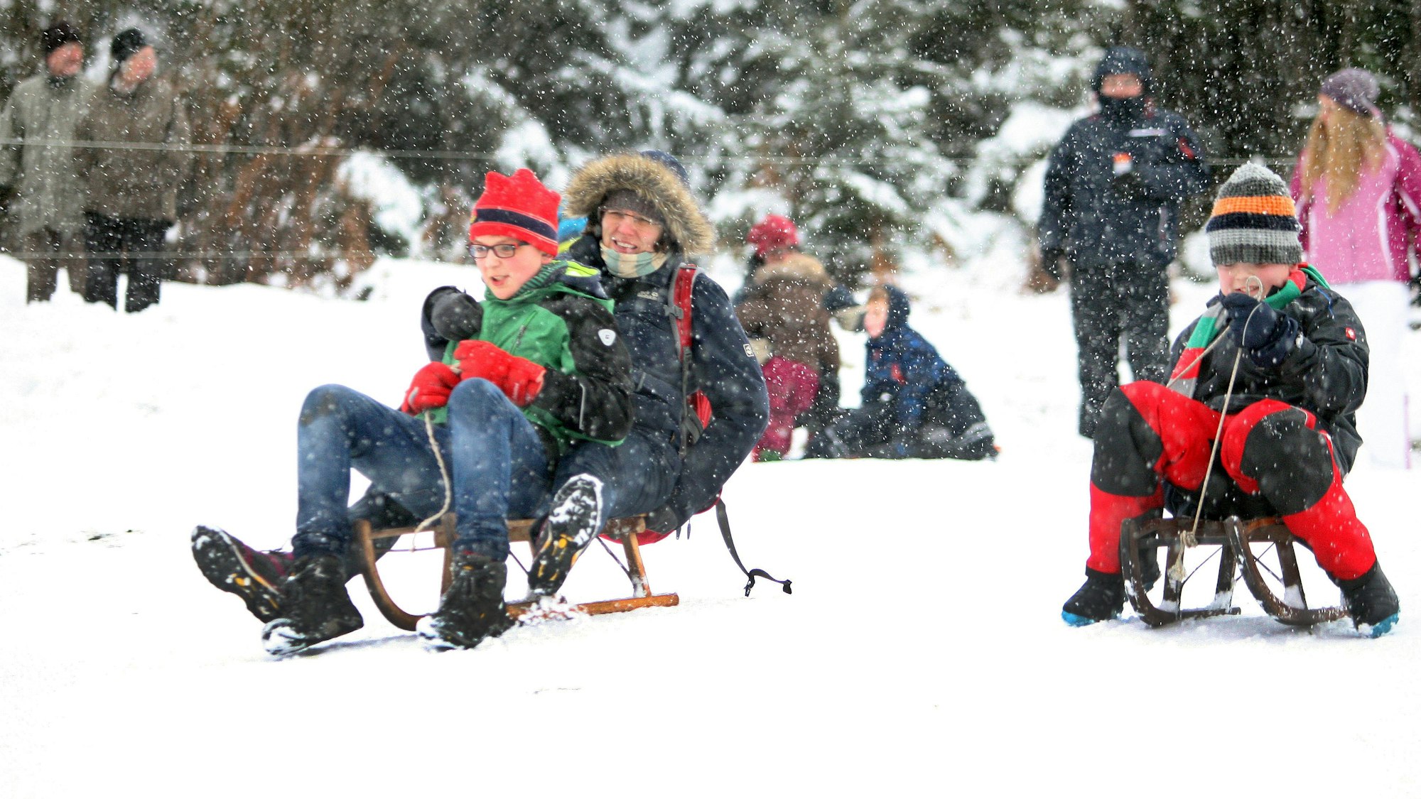 Kinder und Erwachsene fahren mit Schlitten oder spazieren durch den Schnee.