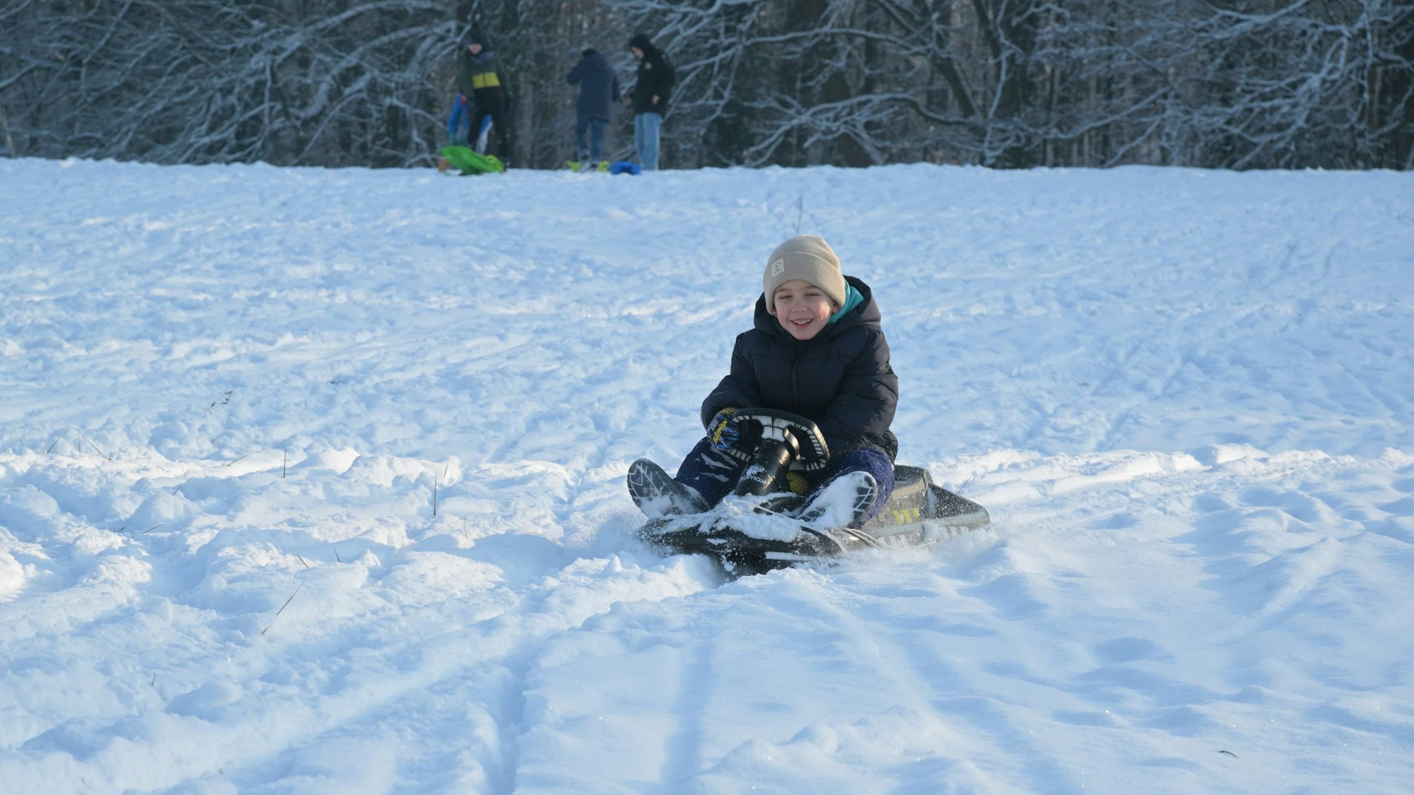 Ein Kind fährt eine verschneite Wiese auf einem Lenkbob herunter.