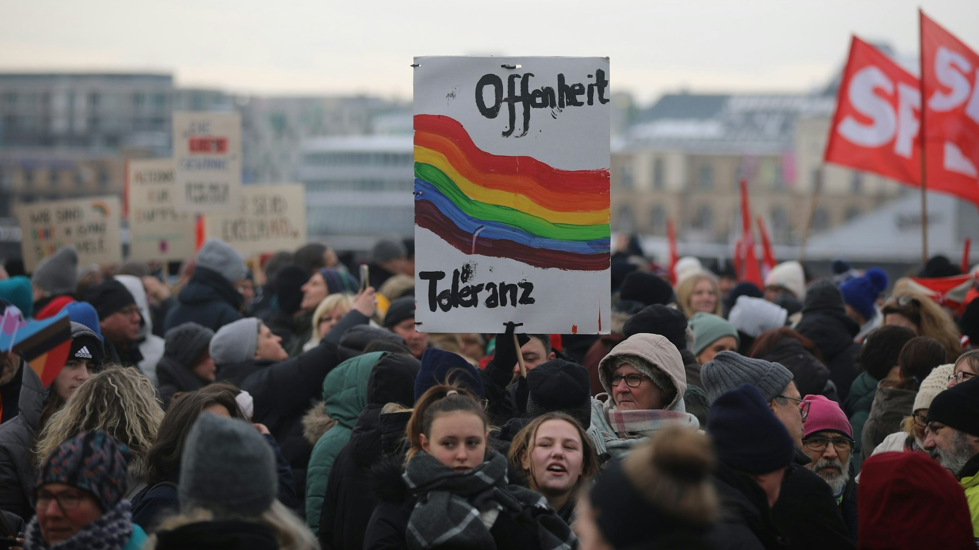 In der Masse von vielen Menschen ist ein Schild mit „Offenheit“ und „Toleranz“ und einem Regenbogen zu sehen.