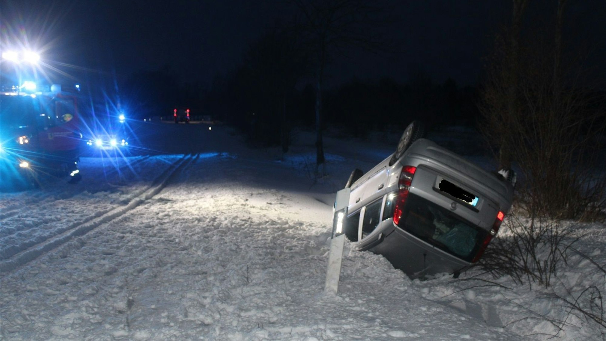 Der Wagen der Unfallfahrerin liegt auf dem Dach im Graben. Auf der verschneiten Straße stehen die Fahrzeuge des Rettungsdienstes.