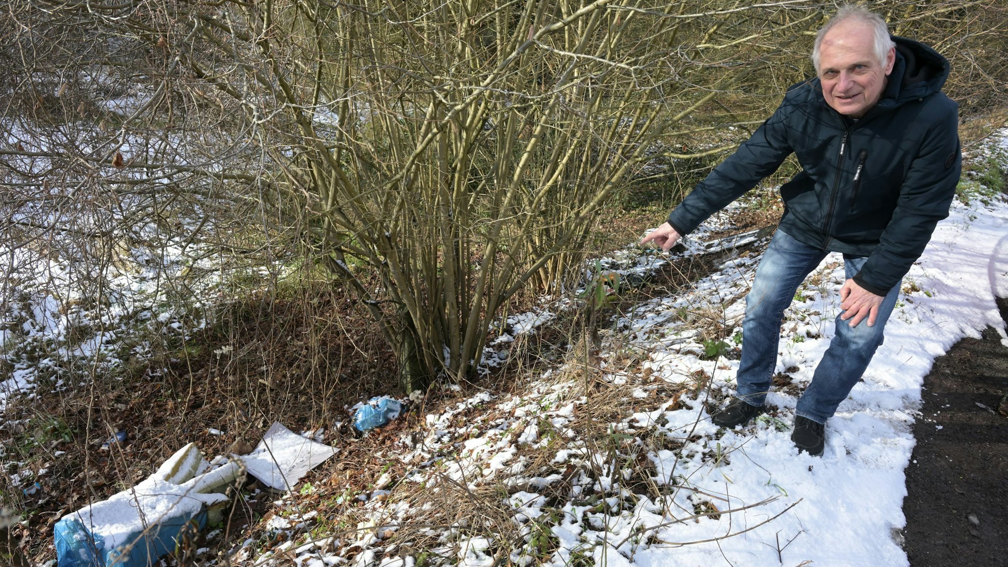 Ein Mann zeigt auf Plastiktüten voller Müll an einer Böschung in Overath-Untereschbach.