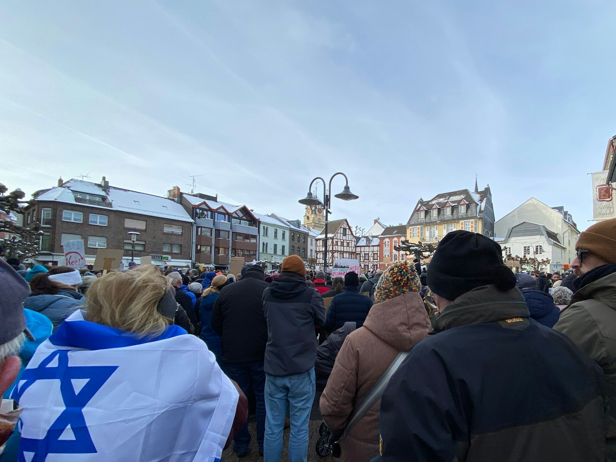 Menschen lauschen einer Kundgebung. Eine Frau trägt eine Israelflagge als Umhang.