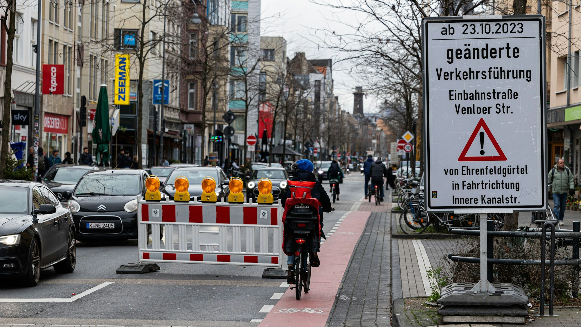 Autos und ein Fahrradfahrer auf der Venloerstraße neben dem Schild, dass die geänderte Verkehrsführung ankündigt.