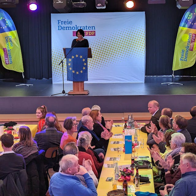Eine Veranstaltung der FDP; auf der Bühne streht eine Frau am Rednerpult hinter einer Europafahne.