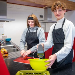 Das Bild zeigt Celina und Jakob in der Schulküche der Zülpicher Hauptschule. Celina schneidet einen Apfel, Jakob hat einen Mixer in der Hand.