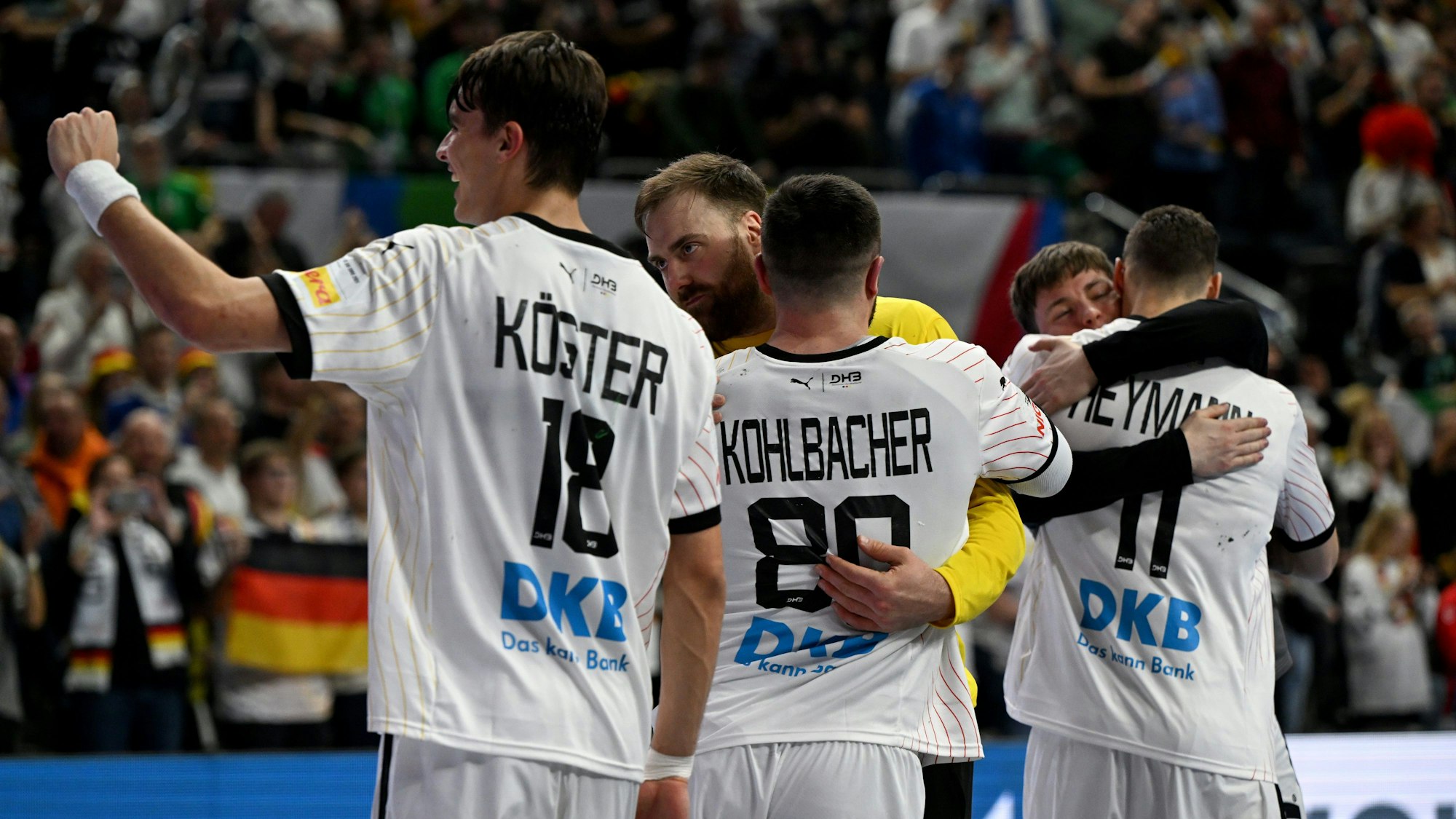 Die deutsche Handballmannschaft umarmt sich und jubelt vor einem unscharfen Publikum im Hintergrund.