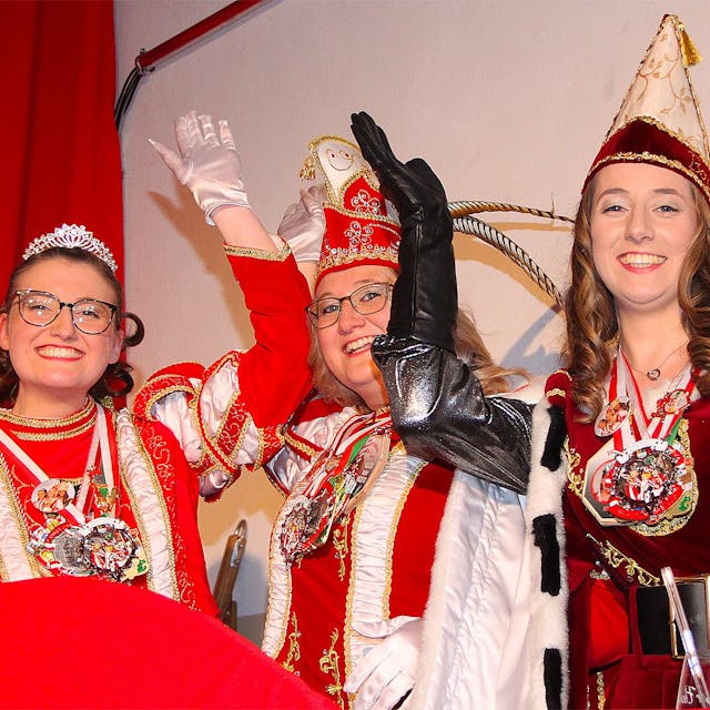 Die drei Frauen, die das Dreigestirn bilden, lachen fröhlich in die Kamera. Sie tragen jeweils mehrere Karnevalsorden.