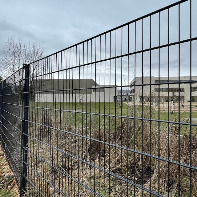 Blick durch einen Zaun auf einen Schulhof mit einer großen Rasenfläche