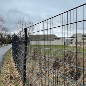 Blick durch einen Zaun auf einen Schulhof mit einer großen Rasenfläche