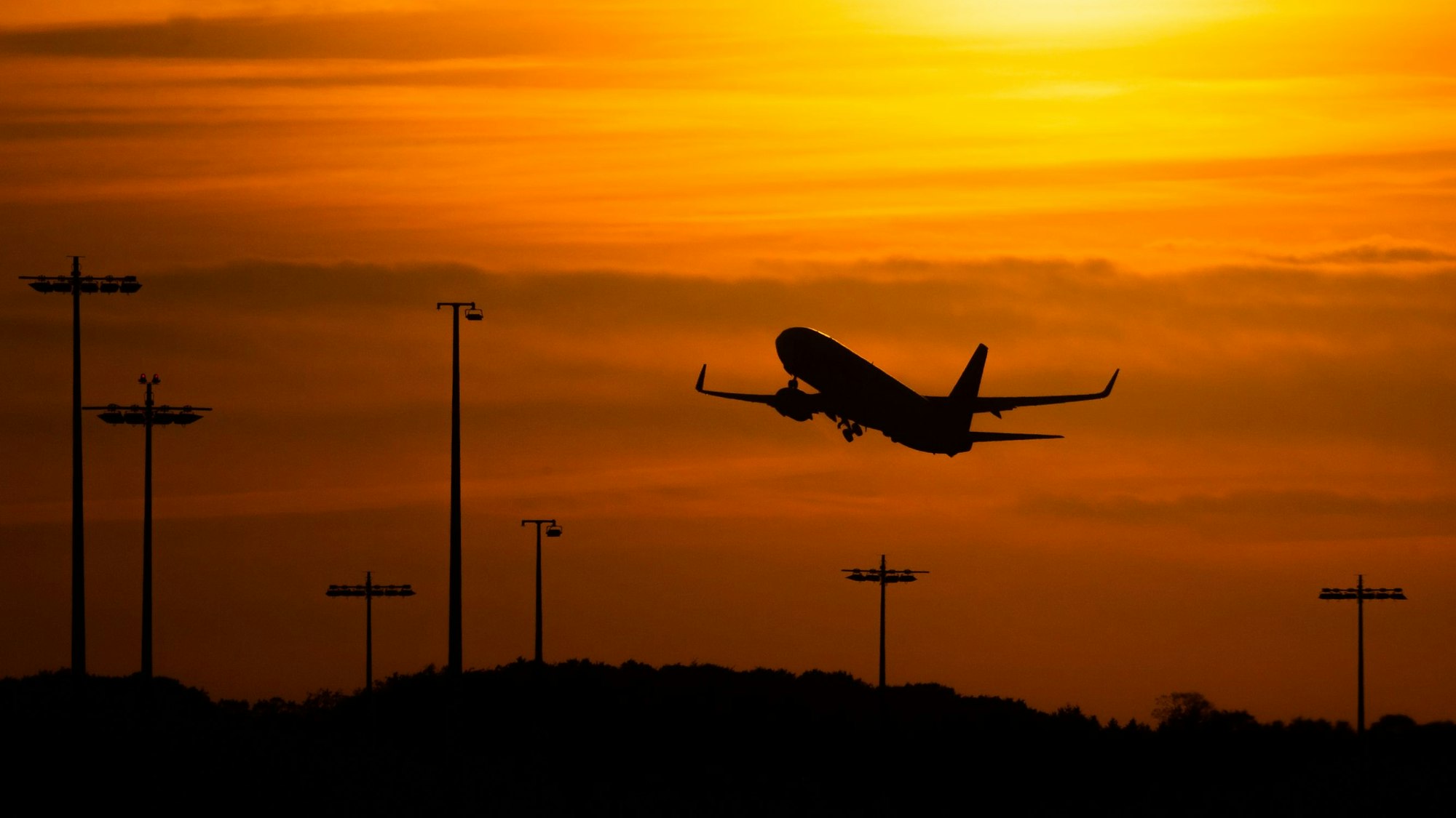 Hamburg: Ein Passagierflugzeug befindet sich am Flughafen von Hamburg im Steigflug vor der untergehenden Sonne.