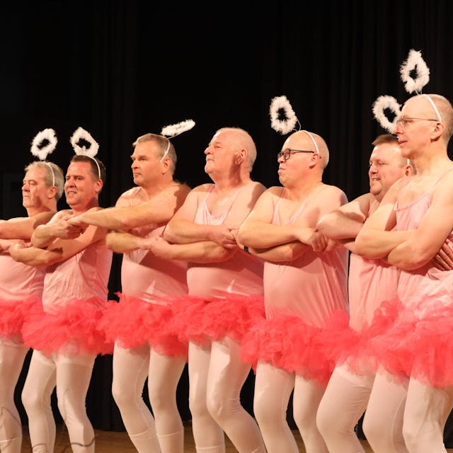 Mehrere Männer tragen rosa Tütüs und tanzen in einer Reihe. Auf dem Kopf tragen sie Heiligenscheine.&nbsp;