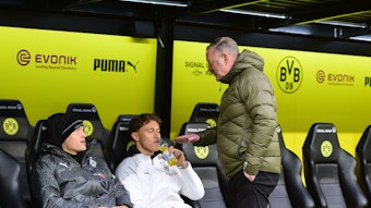 Roland Virkus redet lächelnd mit Luca Netz auf der Bank von Borussia Dortmund.