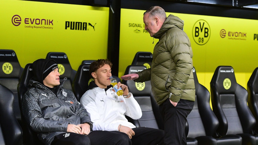 Roland Virkus redet lächelnd mit Luca Netz auf der Bank von Borussia Dortmund.
