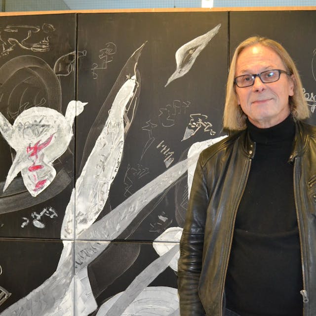 Der Künstler Hans-Heinrich Dittrich (68) mit schwarzem Pullover und Lederjacke steht vor einem seiner Bilder.