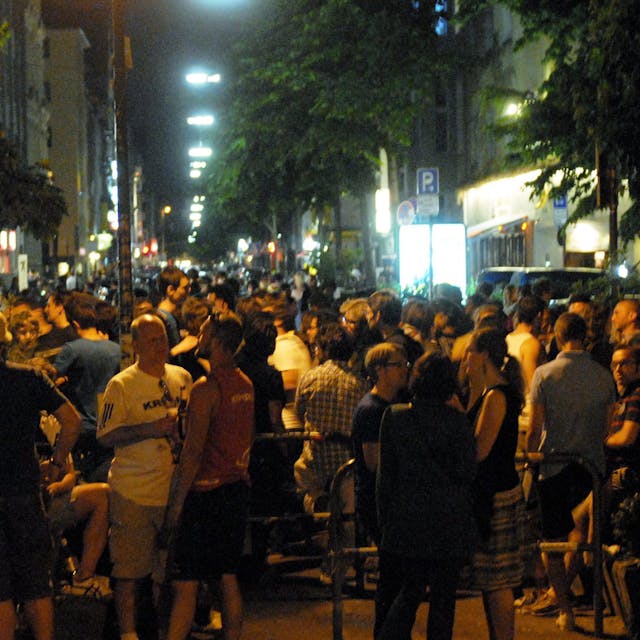 Viele Menschen stehen bei sommerlichen Temperaturen zusammen auf der Straße.
