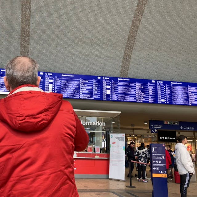 Ein Paar in Winterjacken sucht auf der Anzeigetafel im Kölner Hauptbahnhof nach einem Zug.