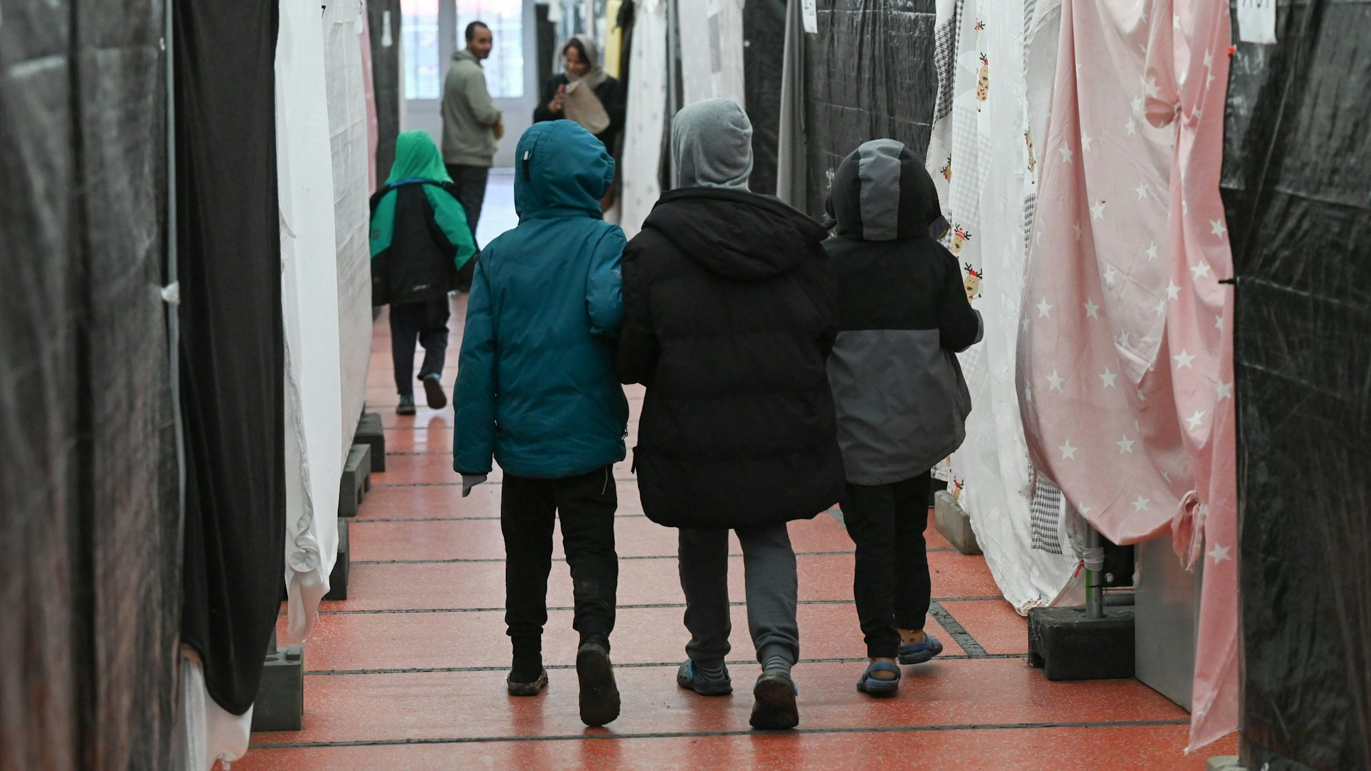 Das Symbolbild zeigt Kinder von hinten, die durch eine Geflüchtetenunterkunft gehen.