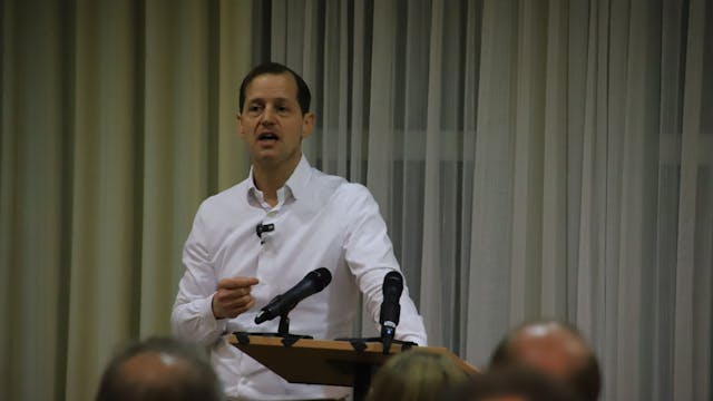 Ein Mann im weißen Hemd und Seitenscheitel steht an einem Rednerpult.