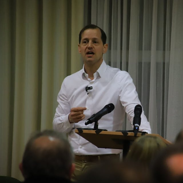 Ein Mann im weißen Hemd und Seitenscheitel steht an einem Rednerpult.