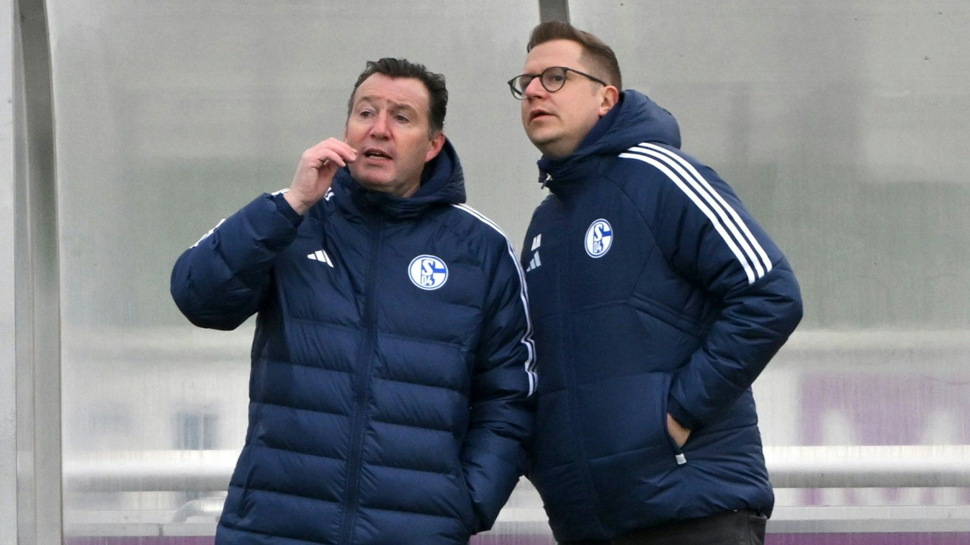 Marc Wilmots und André Hechelmann stehen beim Training von Schalke 04 am Spielfeldrand und unterhalten sich.