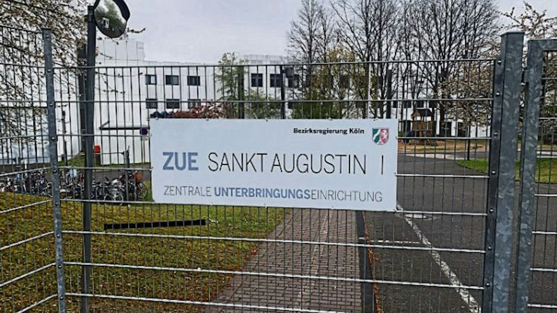 Ein Schild an einem Gitterzaun weist auf die Zentrale Unterbringungseinrichtung des Landes an der Heerstraße in Sankt Augustin hin.