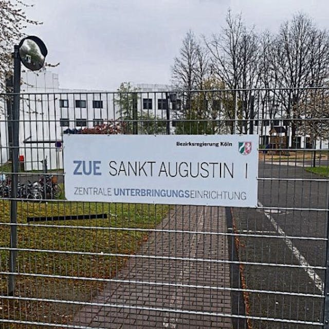 Ein Schild an einem Gitterzaun weist auf die Zentrale Unterbringungseinrichtung des Landes an der Heerstraße in Sankt Augustin hin.