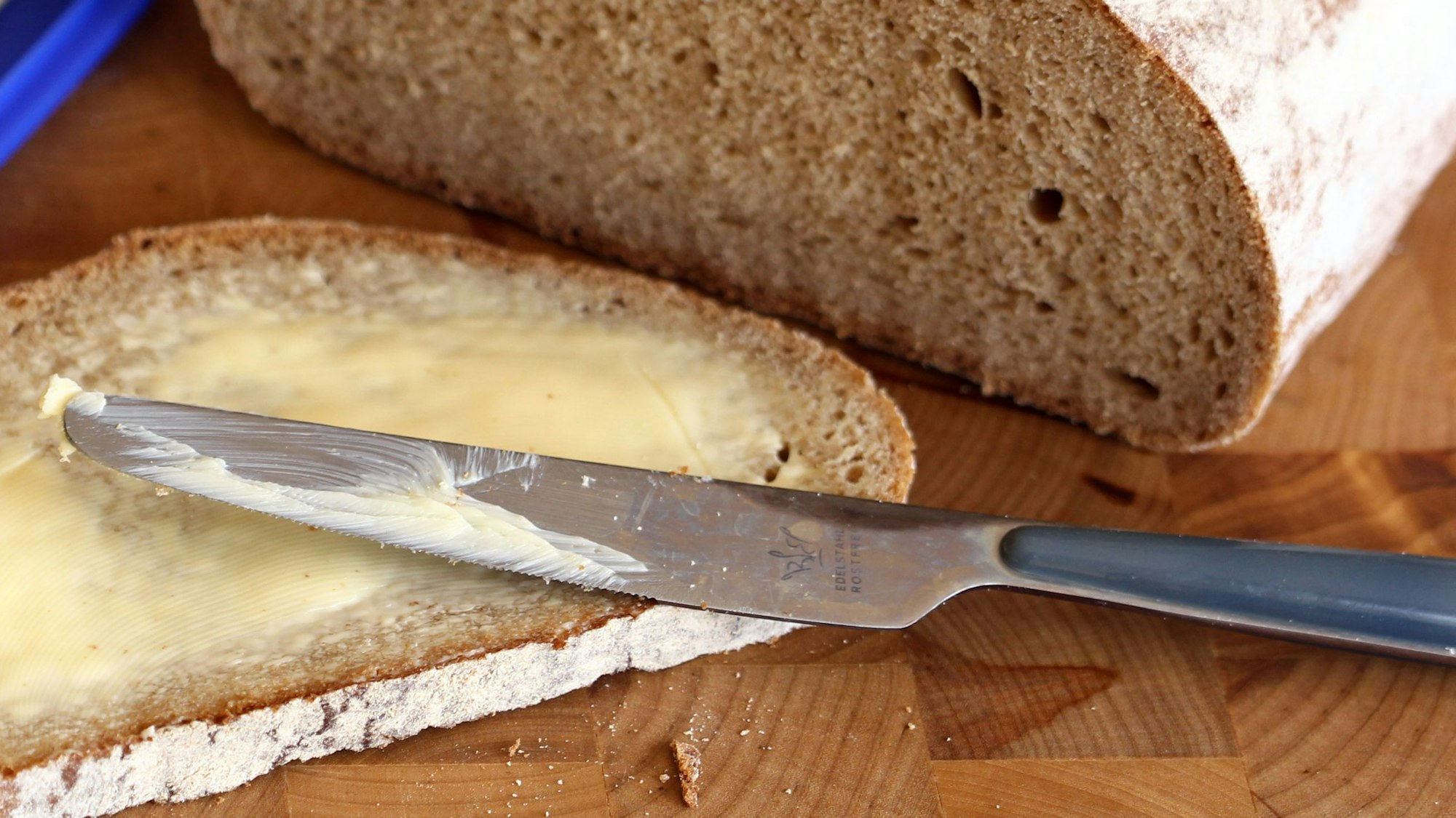 Ein Butterbrot liegt auf einem Frühstücksbrett, darauf das Messer.