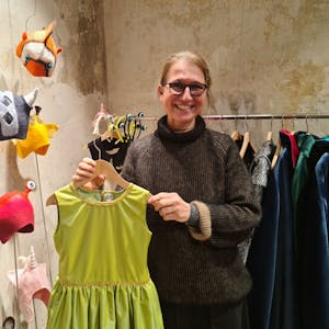 Eine Frau steht in einem Laden, sie zeigt ein grünes Kleid.