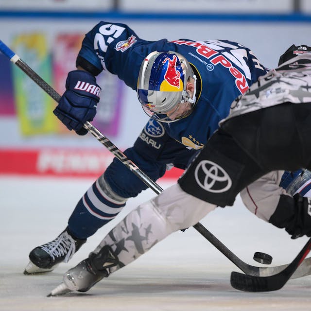 Eishockeyspieler fahren aus gegenübersetzten Richtungen auf einen Puck zu, bei dem sich ihre Schläger treffen.