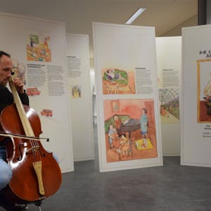 Ein Cello-Spieler sitzt vor Aufstellern.