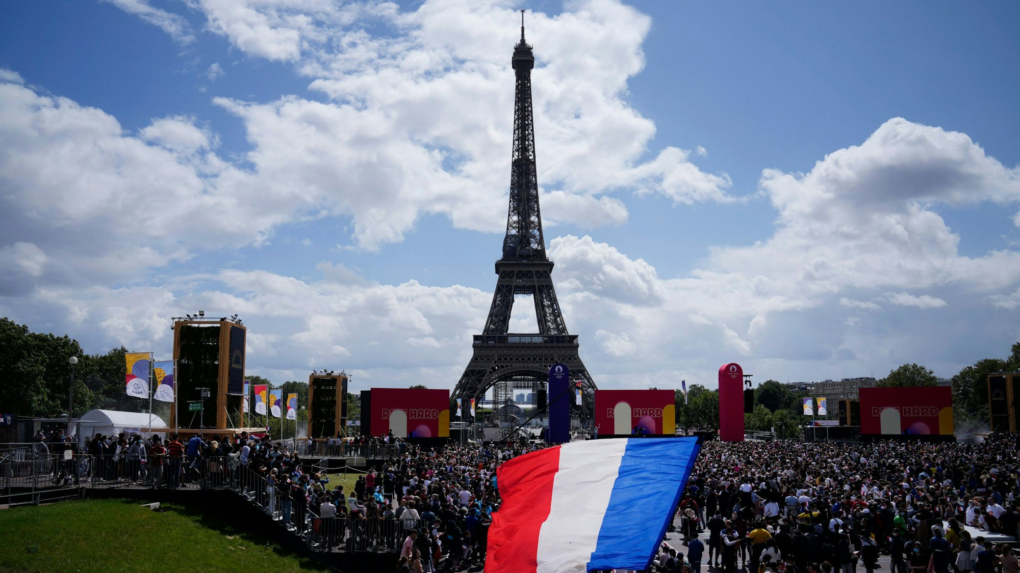 Ein Mann entrollt Fahne in den Farben der französische Nationalflagge in der olympischen Fanzone im Trocadero-Garten vor dem Eiffelturm.