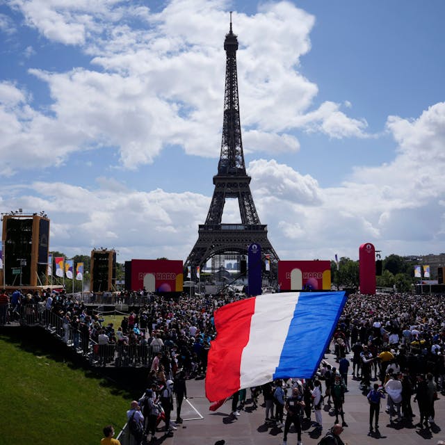Ein Mann entrollt Fahne in den Farben der französische Nationalflagge in der olympischen Fanzone im Trocadero-Garten vor dem Eiffelturm.&nbsp;