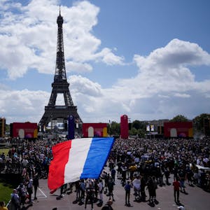 Ein Mann entrollt Fahne in den Farben der französische Nationalflagge in der olympischen Fanzone im Trocadero-Garten vor dem Eiffelturm.&nbsp;
