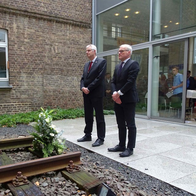 Rheinbachs Bürgermeister Ludger Banken und der Landtagsabgeordnete Oliver Krauß legen ein Gesteck im Innenhof des Rheinbacher Rathauses nieder, vor einer Gedenkstätte der Opfer des Nationalsozialismus.