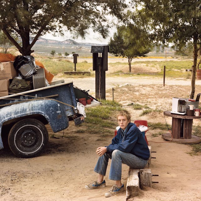 Ein Junge sitzt auf einem Campingplatz neben einem vollgepackten Lastwagen.