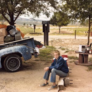 Ein Junge sitzt auf einem Campingplatz neben einem vollgepackten Lastwagen.